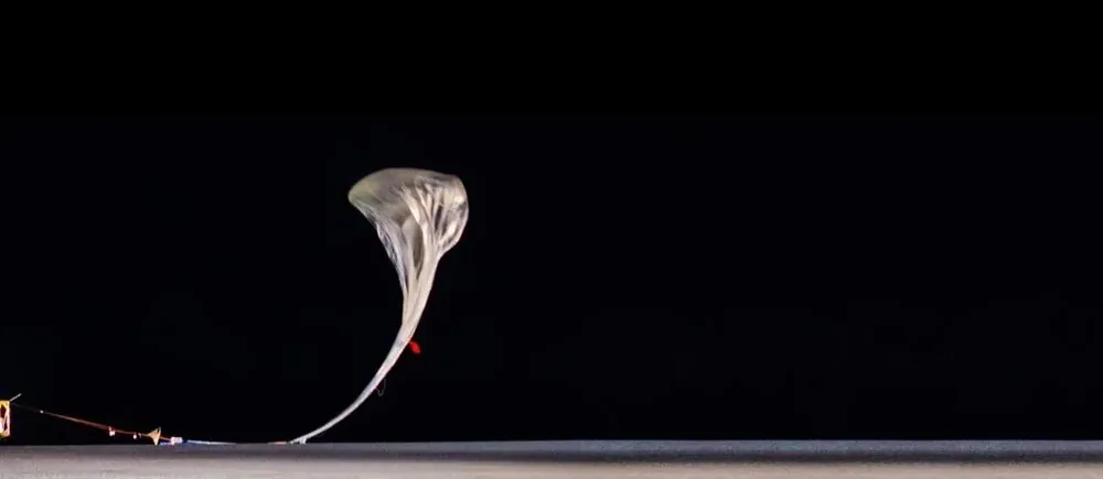 A stratospheric balloon being released at night beside its launch vehicle