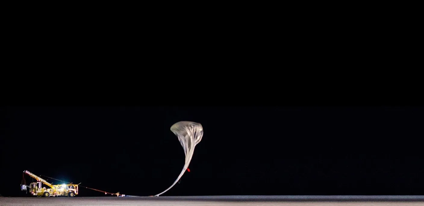 A stratospheric balloon being released at night beside its launch vehicle