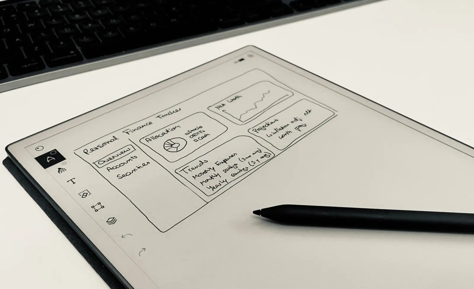 A reMarkable Paper Pro on a desk showing a hand-drawn finance dashboard sketch, with its pen lying across the screen